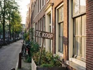 Traditioneel Nederlands bakstenen huis met witte kozijnen en "Te Koop" bord in de voortuin, typische Amsterdamse architectuur