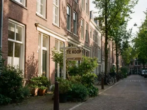 Traditioneel Nederlands bakstenen herenhuis met witte kozijnen en "Te Koop" bord in voortuin, warme middagzon