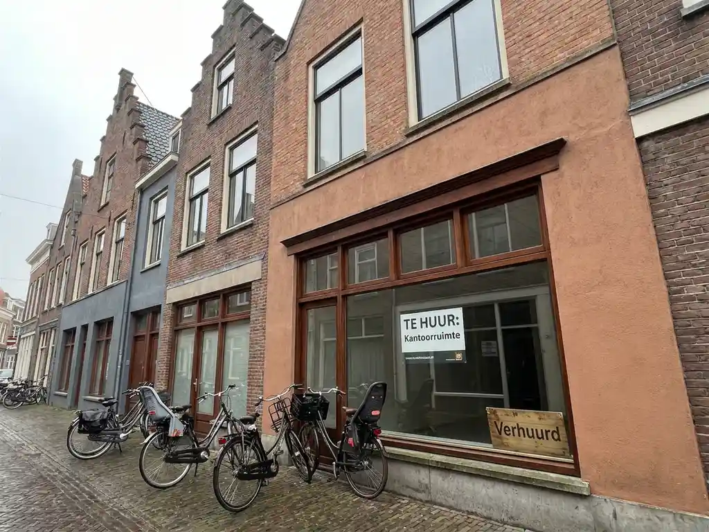 Verhuurd Nederlands bedrijfspand met bakstenen gevel, verhuurbordje in het raam en fietsen geparkeerd buiten.